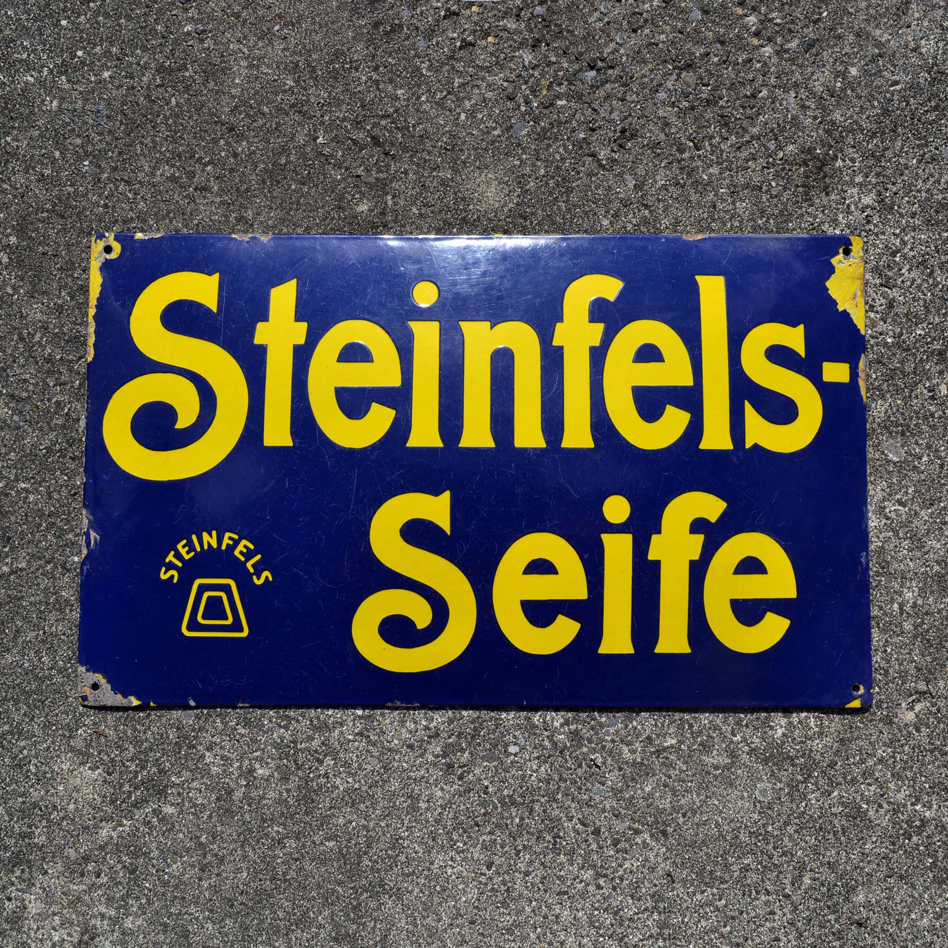 Plaque émaillée pour le savon Steinfels. D’origine Suisse alémanique. Bombée, vers 1910-20. Fond bleu, avec lettrage jaune. Schweizer Emailschild.