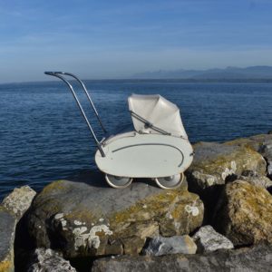 Poussette Helvétia beige des années 1950, avec caisse en bois. Petit modèle pour poupée, avec capote pliante, habillage en toile cirée banche.