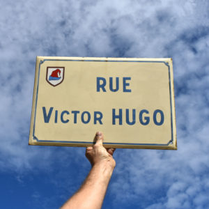 Plaque de rue émaillée française. Rue Victor Hugo. Avec fond beige et lettrage bleu. Blason de la ville de Guebviller.